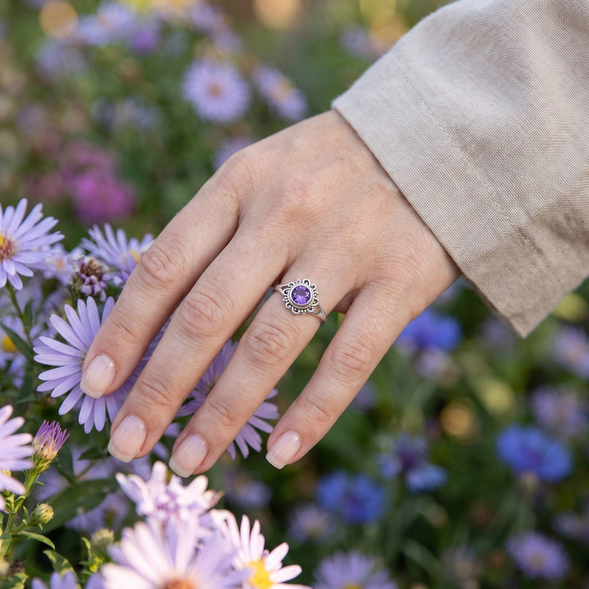 Silberring mit Amethyst an der Hand zwischen Blumen