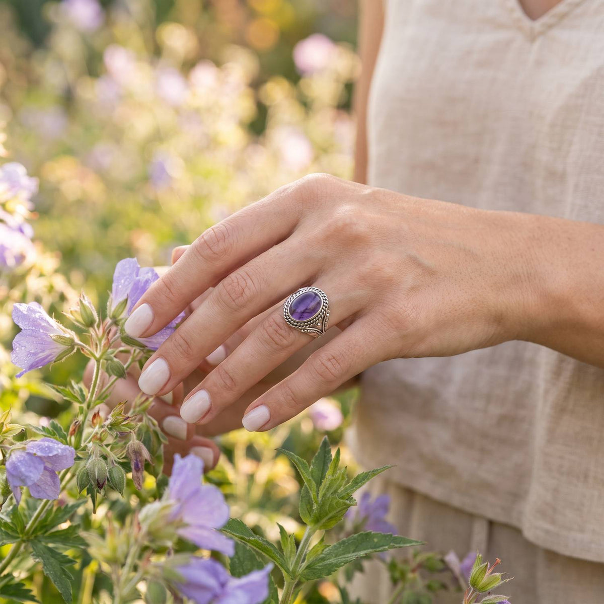 Silberring mit Amethyst an der Hand zwischen Blumen