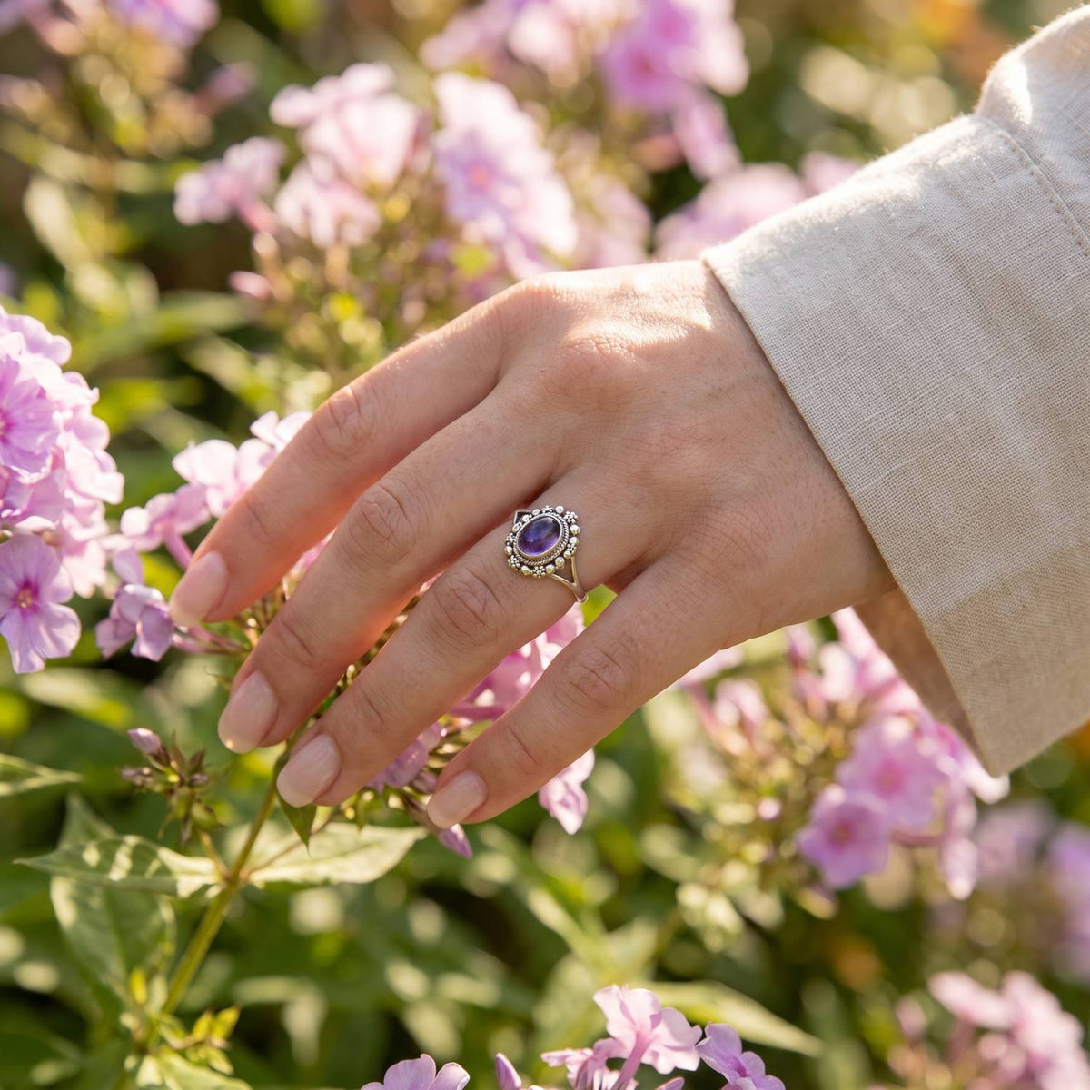 Silberring mit Amethyst an der Hand zwischen Blumen