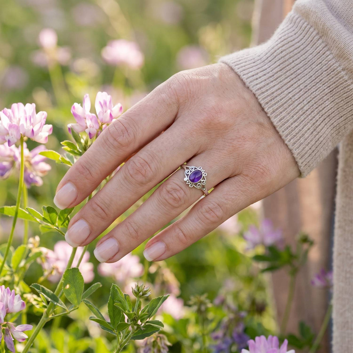 Silberring mit Amethyst an der Hand zwischen Blumen