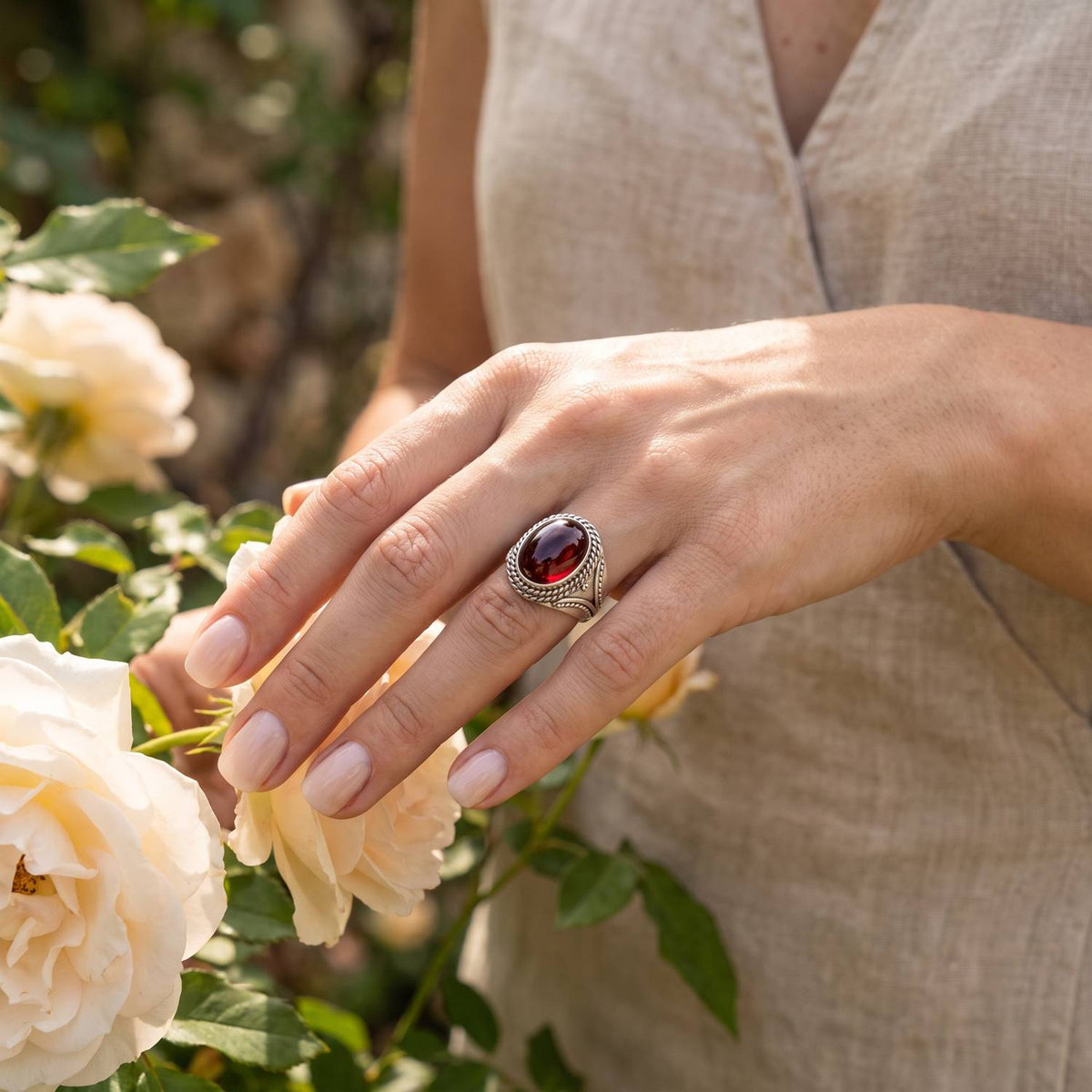 Silberring mit Granat an der Hand zwischen Blumen