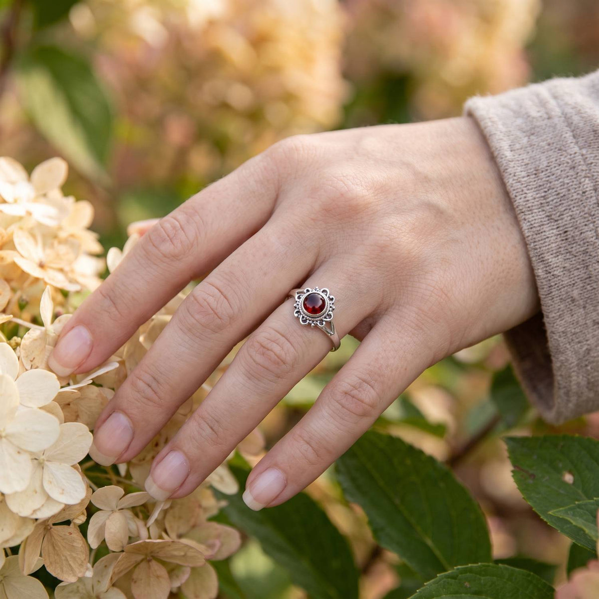 Silberring mit Granat an der Hand zwischen Blumen