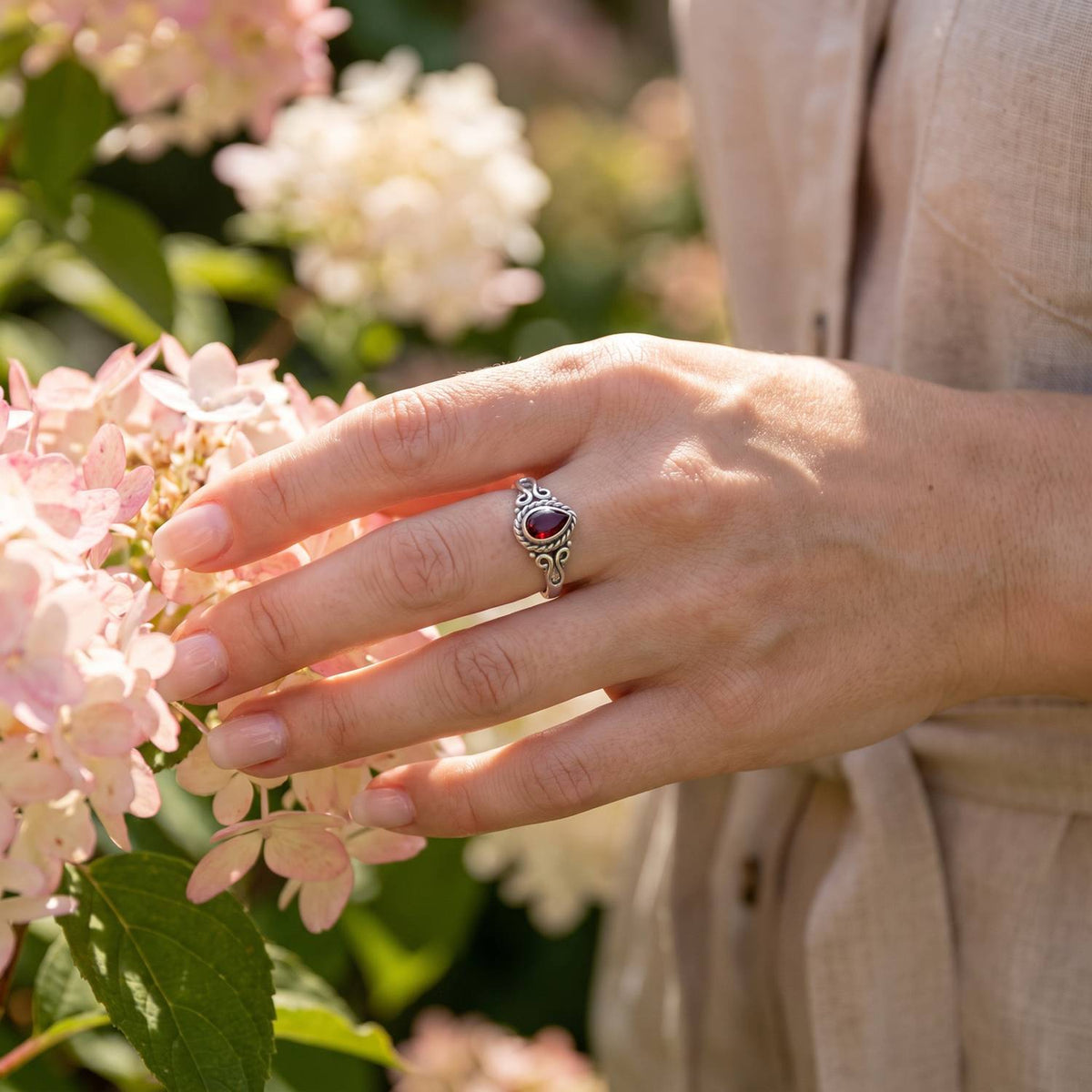 Silberring mit Granat an der Hand zwischen Blumen