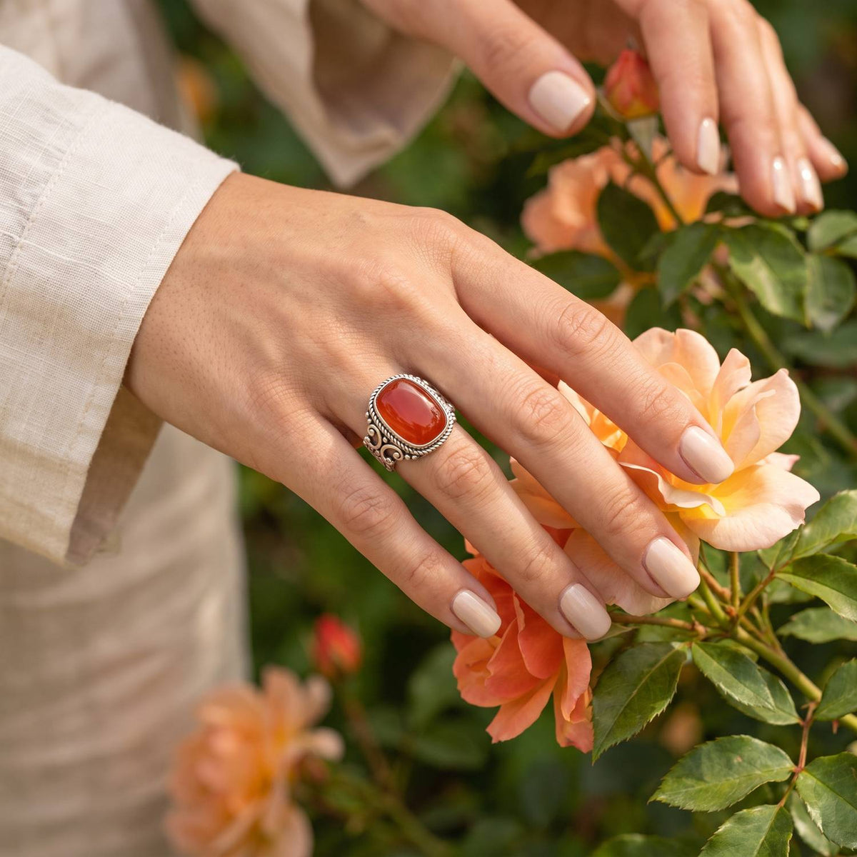 Silberring mit Karneol an der Hand zwischen Blumen