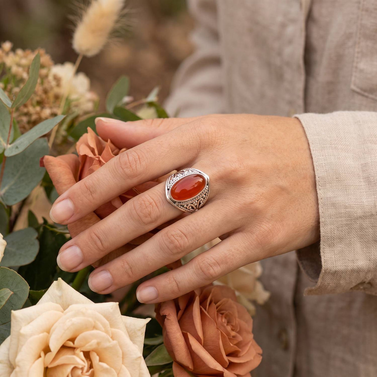 Silberring mit Karneol an der Hand zwischen Blumen