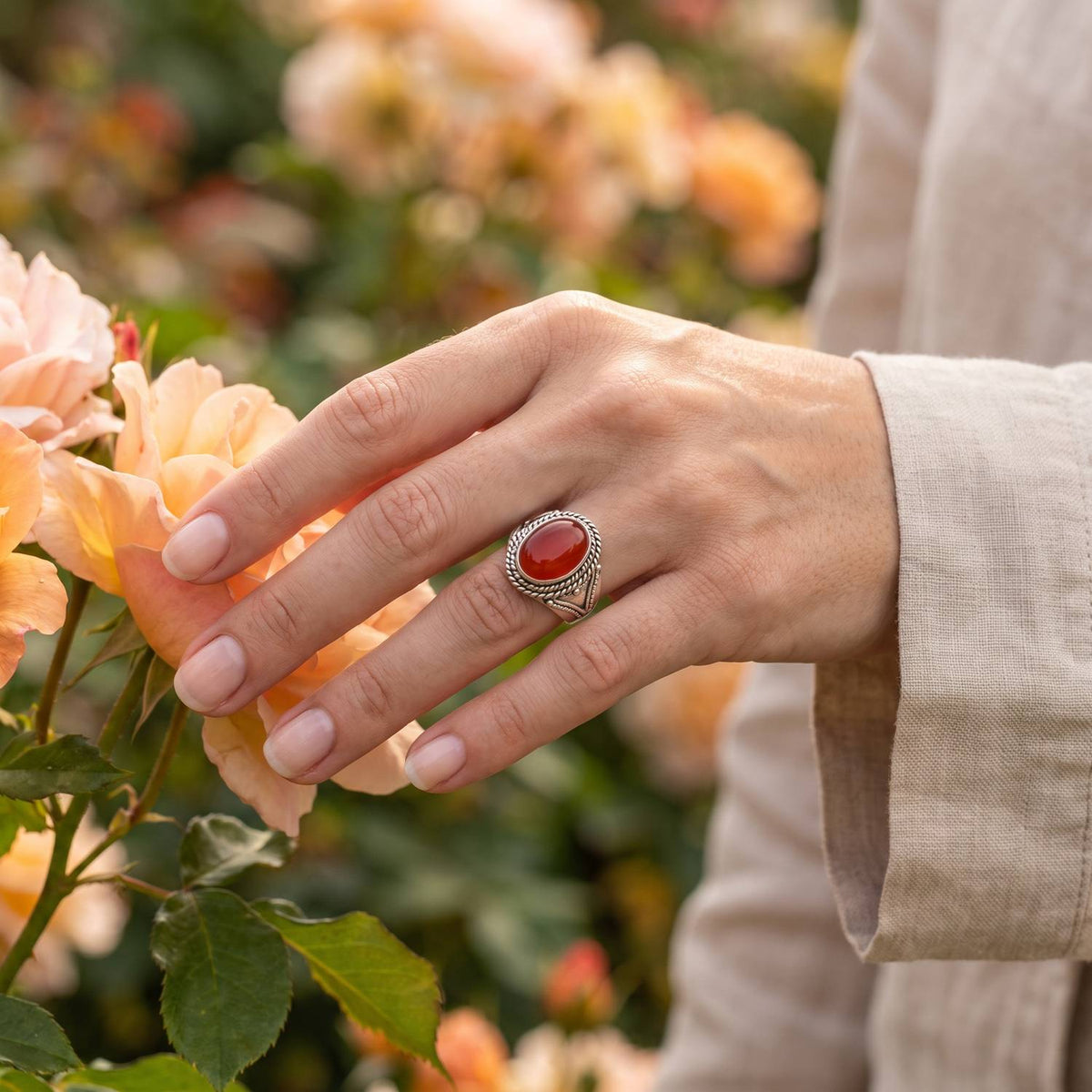 Silberring mit Karneol an der Hand zwischen Blumen