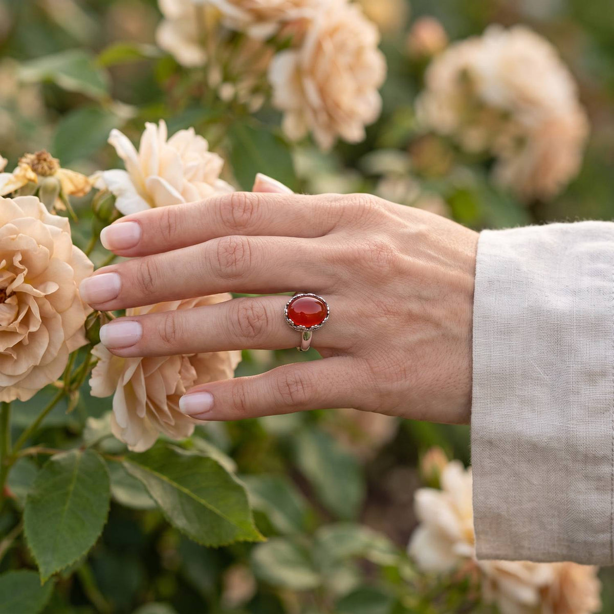 Silberring mit Karneol an der Hand zwischen Blumen