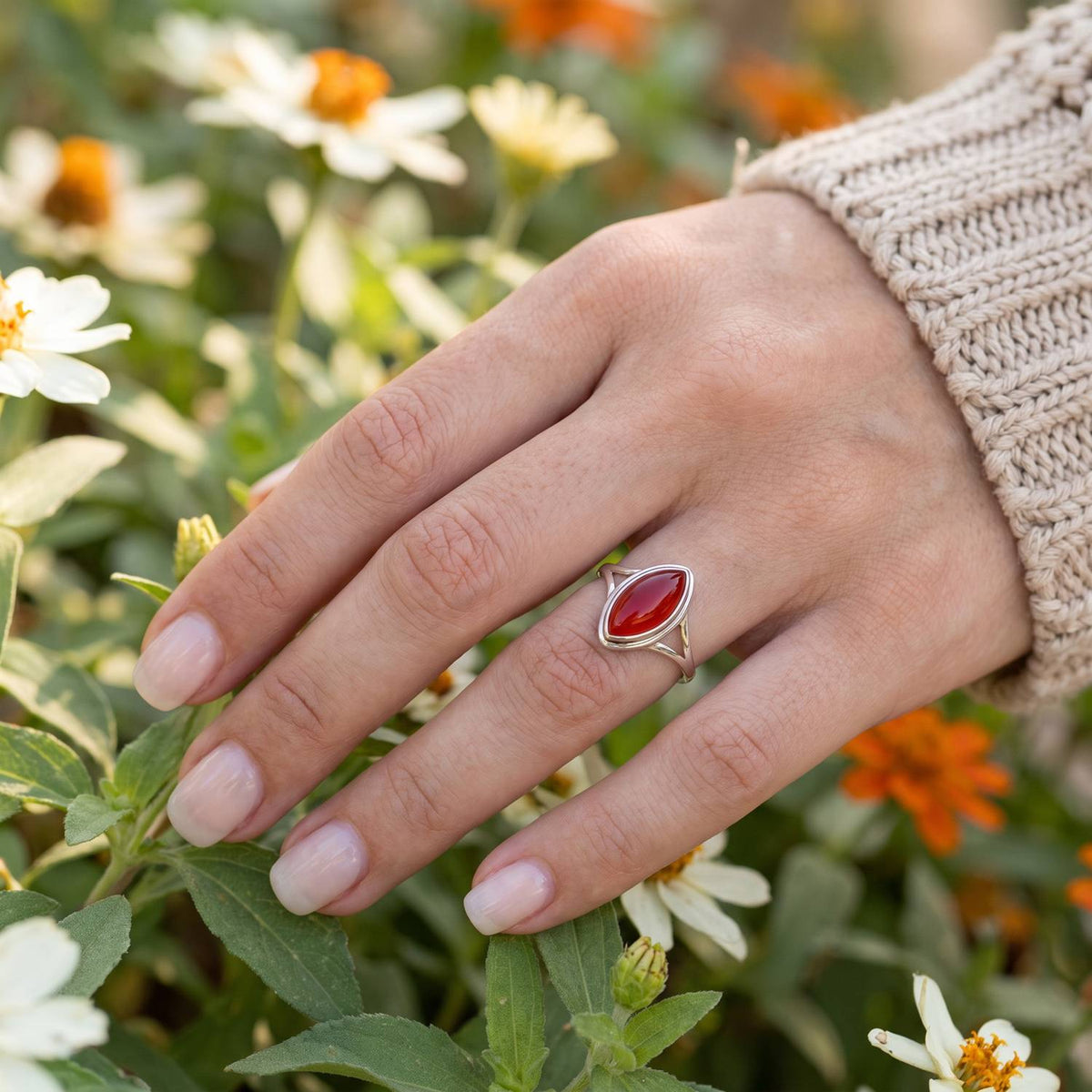 Silberring mit Karneol an der Hand zwischen Blumen