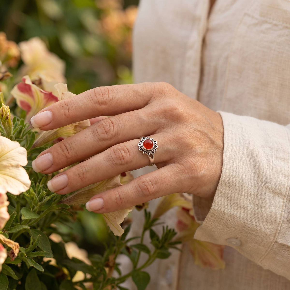 Silberring mit Karneol an der Hand zwischen Blumen