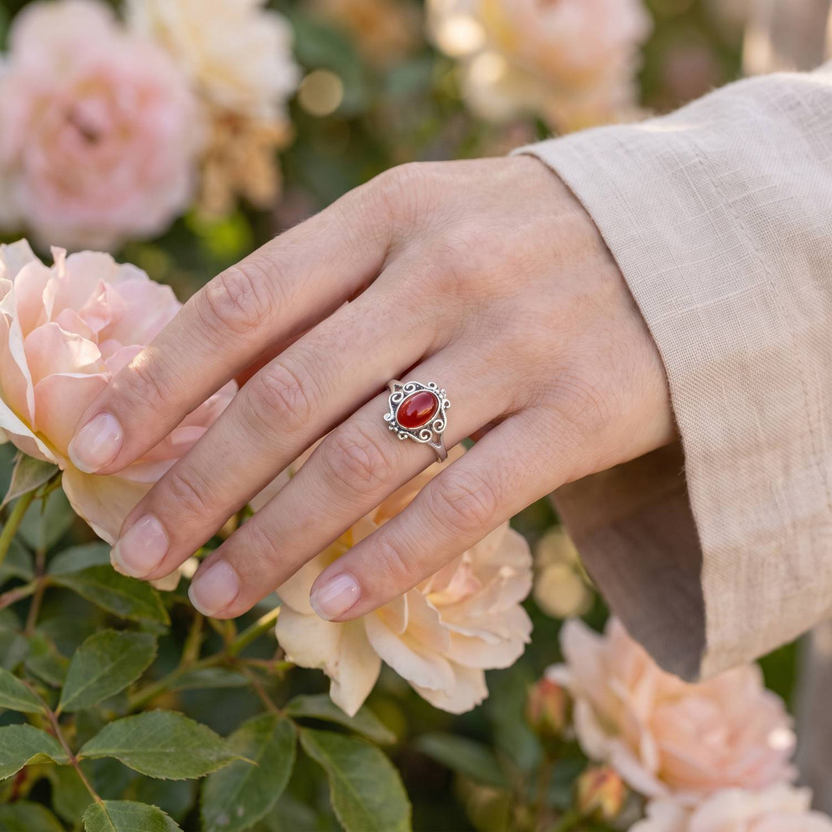 Silberring mit Karneol an der Hand zwischen Blumen