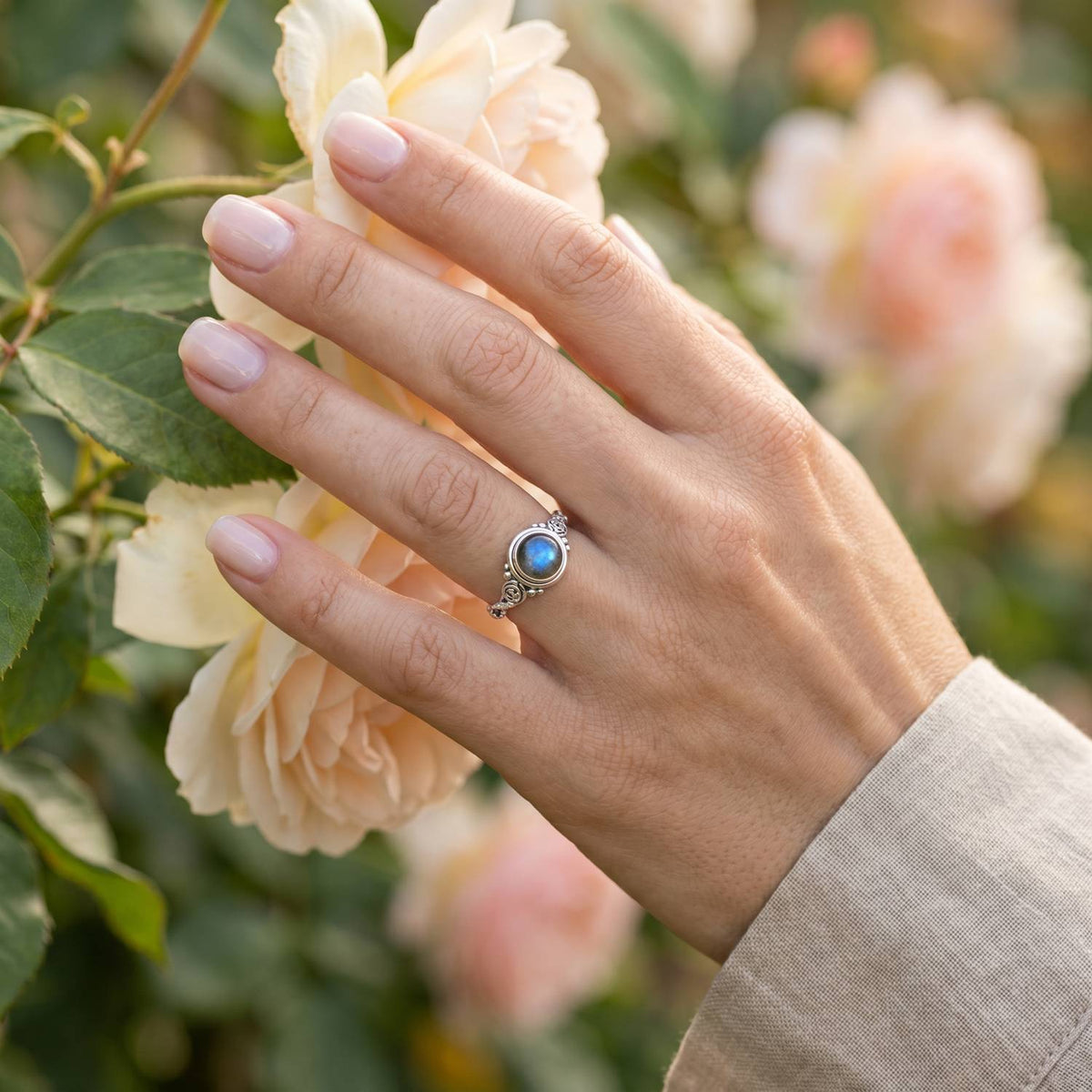 Silberring mit Labradorit an der Hand zwischen Blumen