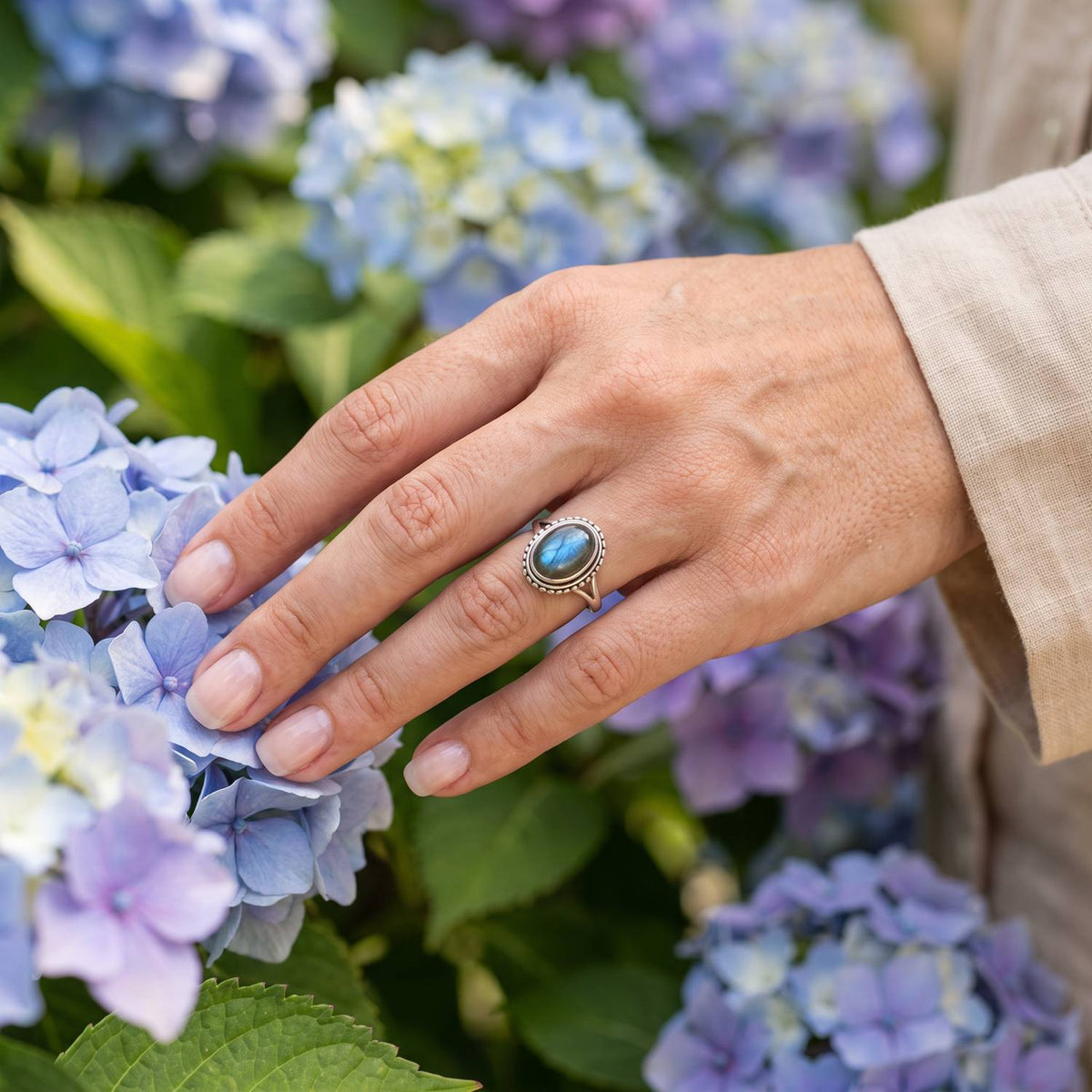 Silberring mit Labradorit an der Hand zwischen Blumen