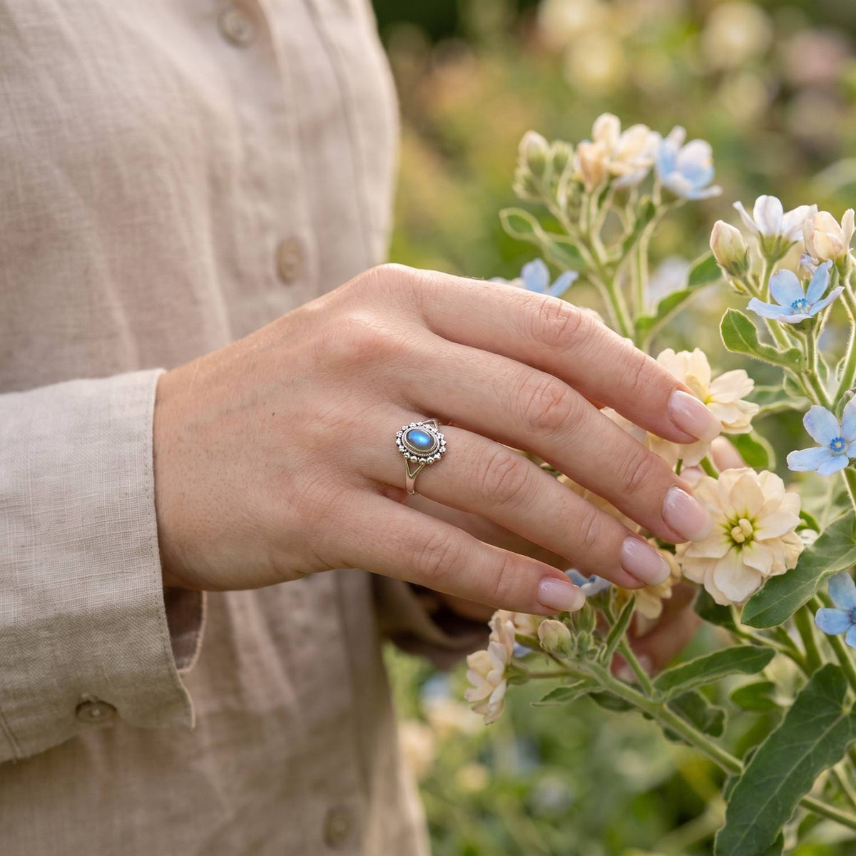 Silberring mit Labradorit an der Hand zwischen Blumen