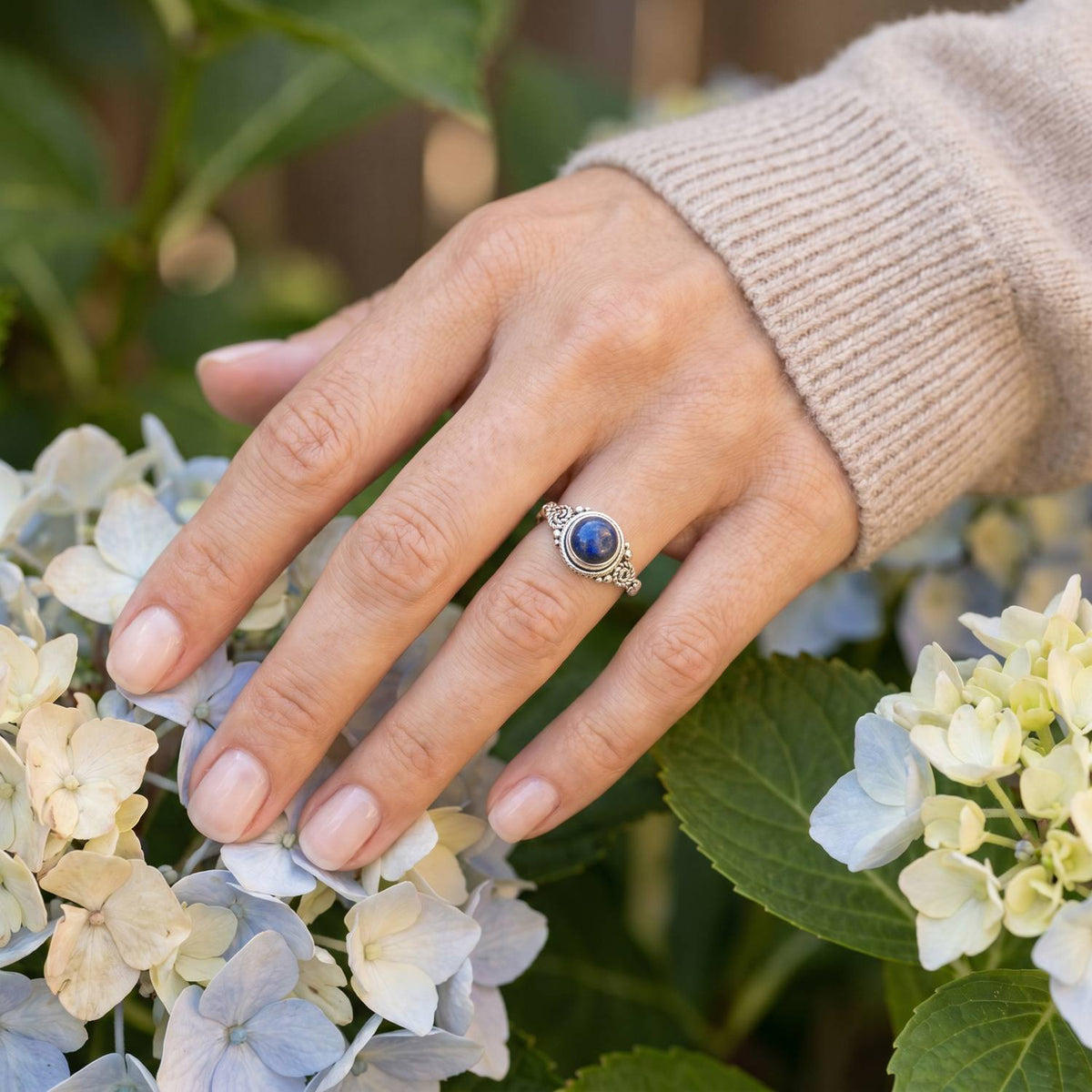 Silberring mit Lapislazuli an der Hand zwischen Blumen
