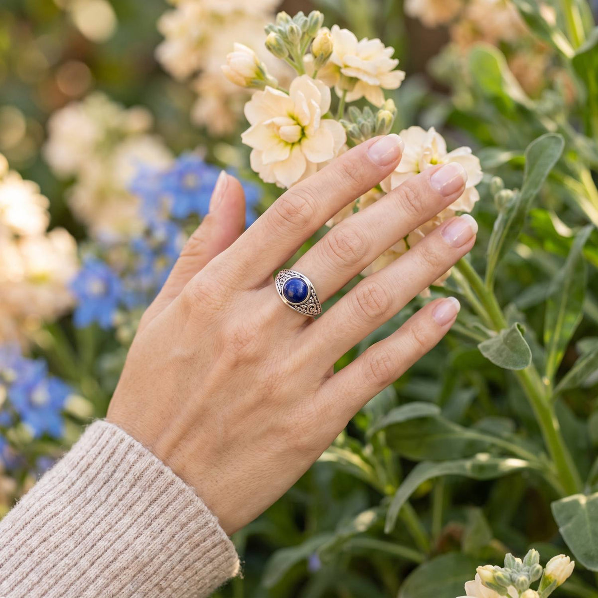 Silberring mit Lapislazuli an der Hand zwischen Blumen