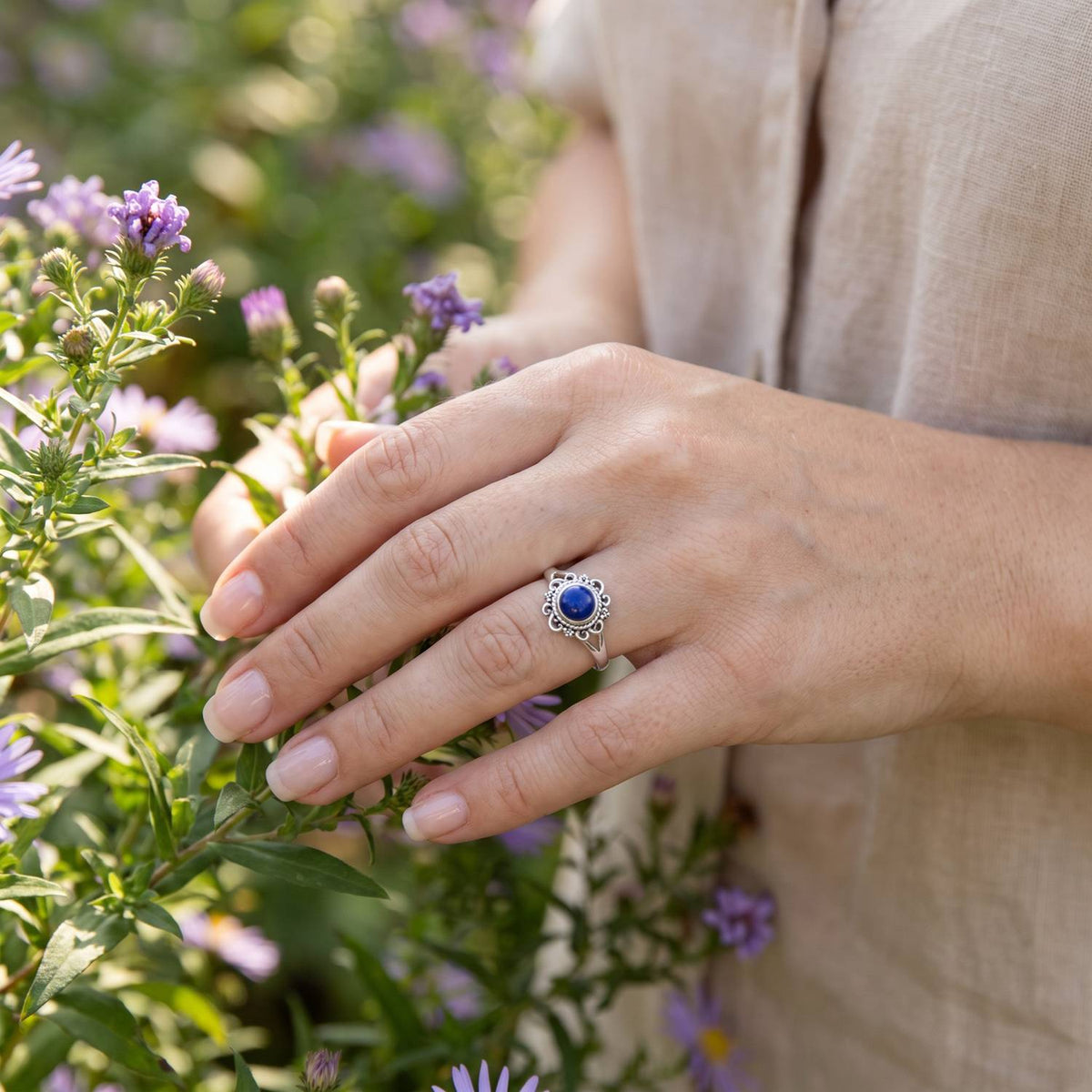 Silberring mit Lapislazuli an der Hand zwischen Blumen