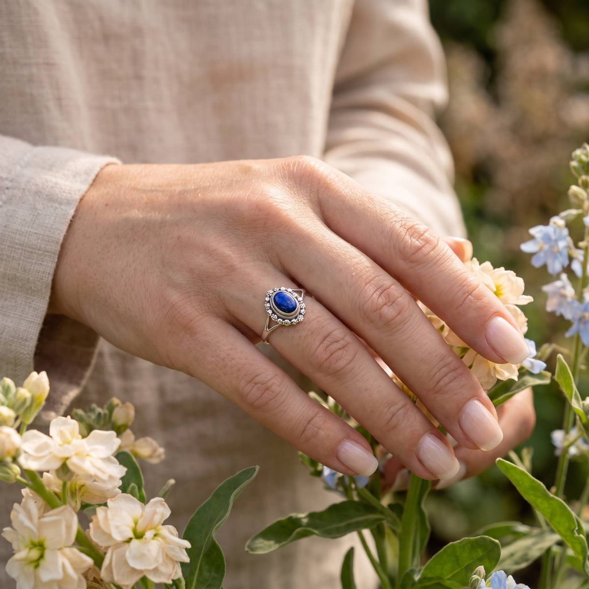 Silberring mit Lapislazuli an der Hand zwischen Blumen