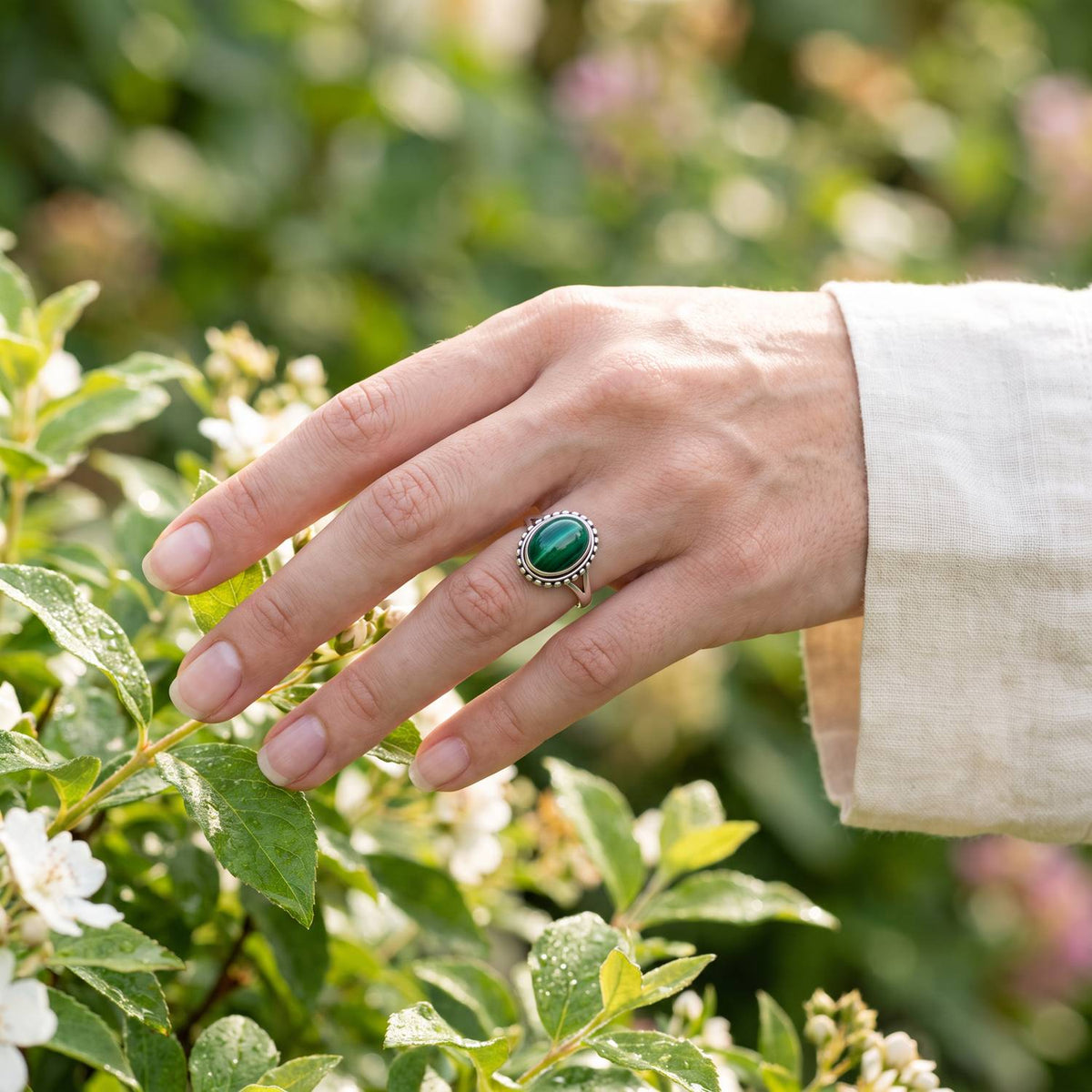 Silberring mit Malachit an der Hand zwischen Blumen
