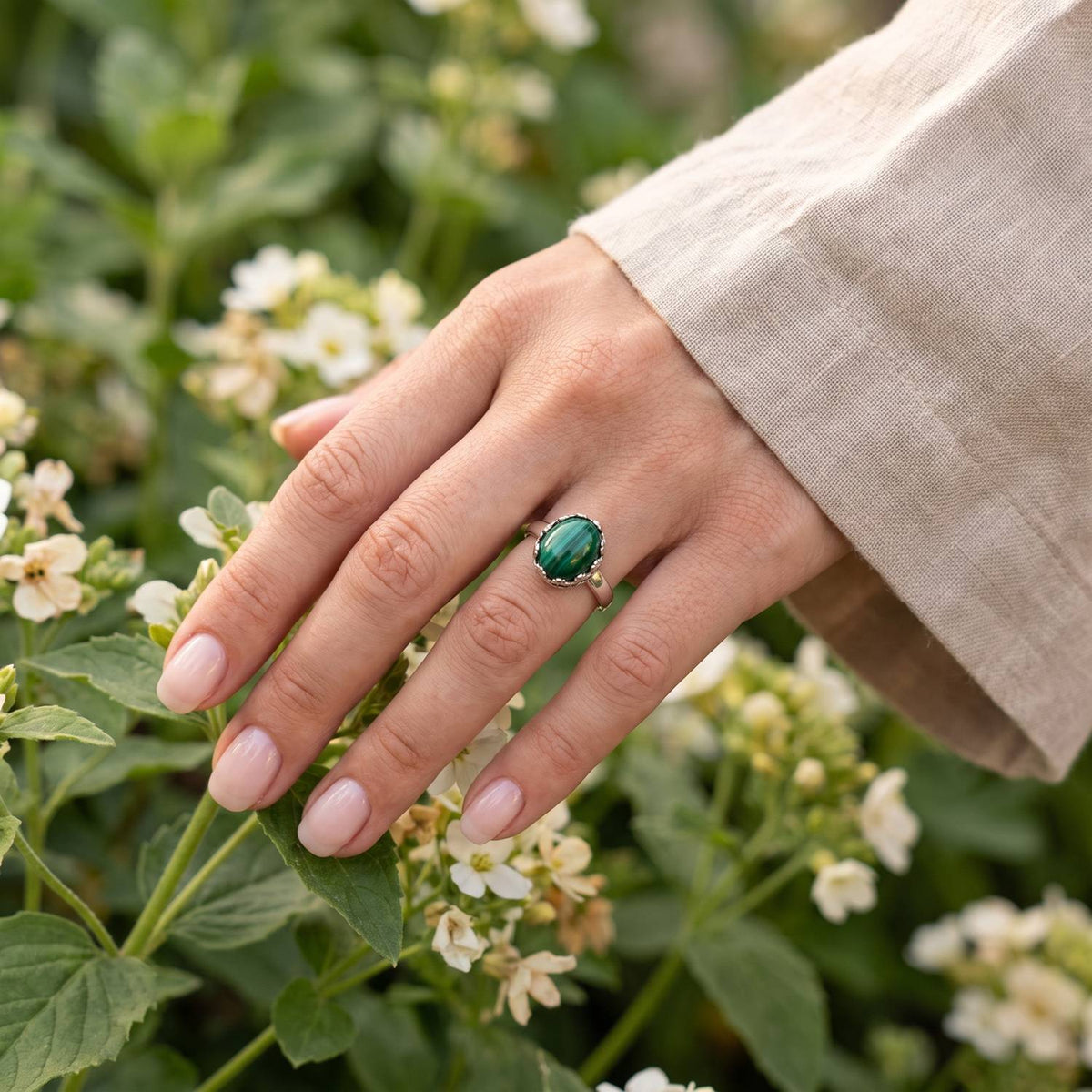 Silberring mit Malachit an der Hand zwischen Blumen