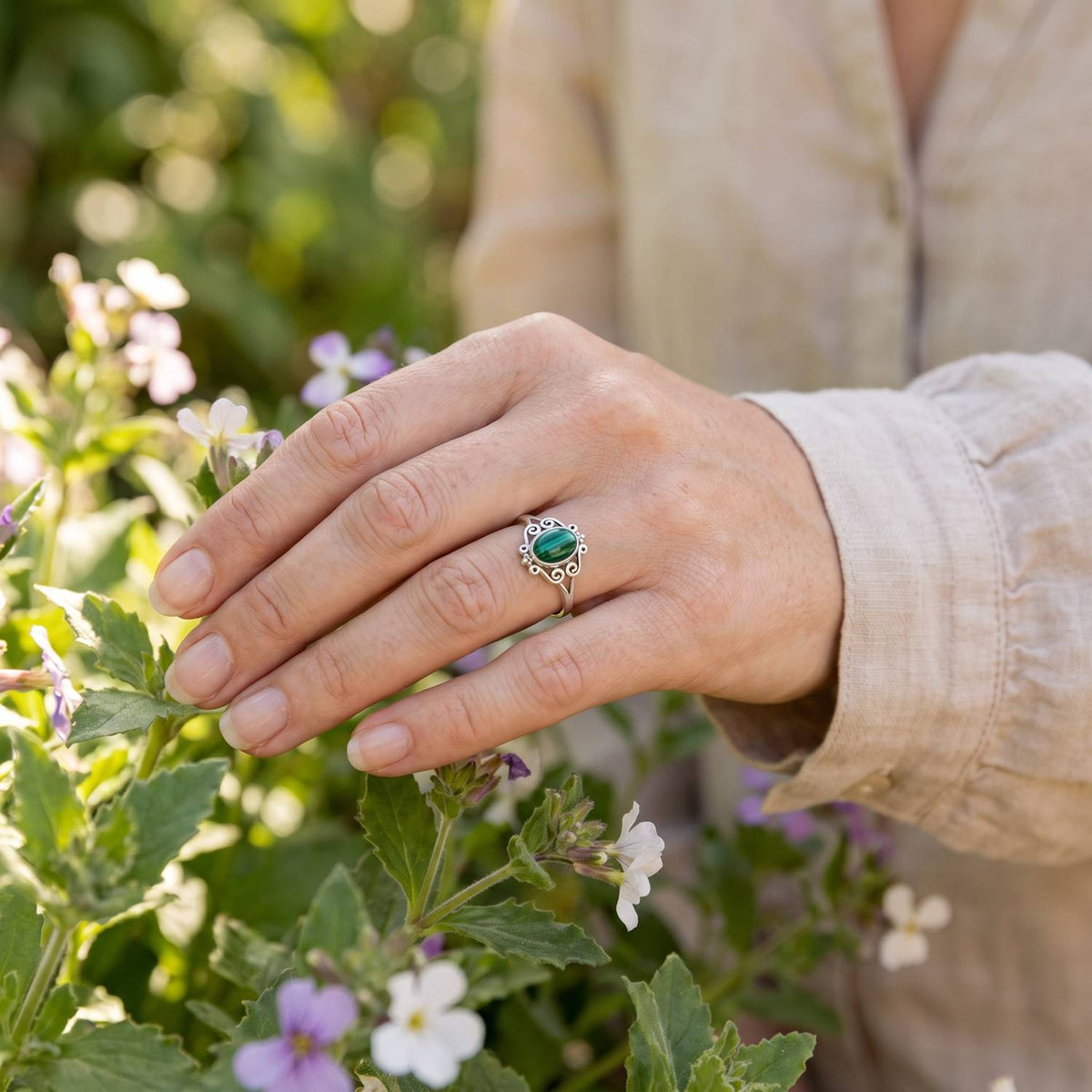 Silberring mit Malachit an der Hand zwischen Blumen