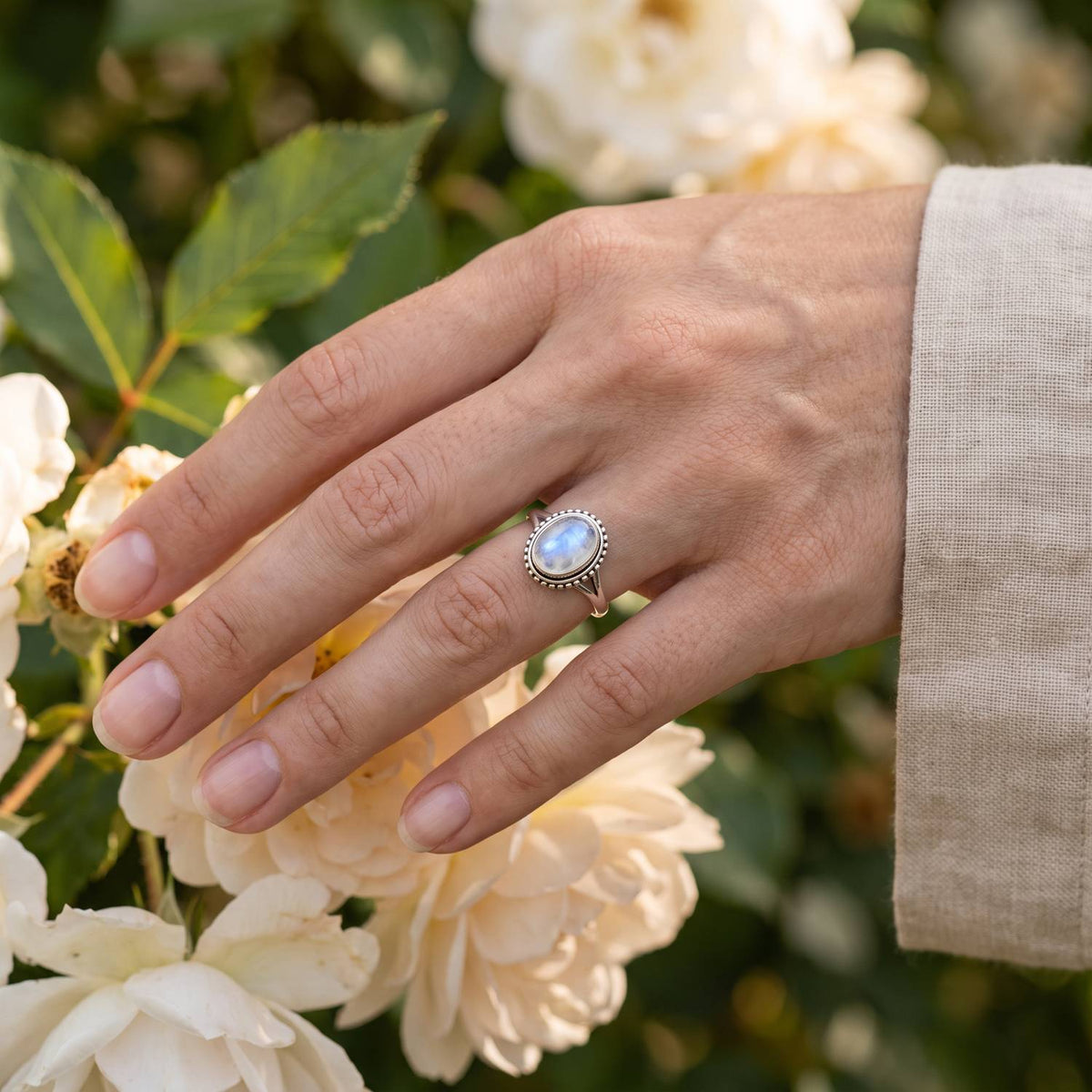Silberring mit Mondstein an der Hand zwischen Blumen