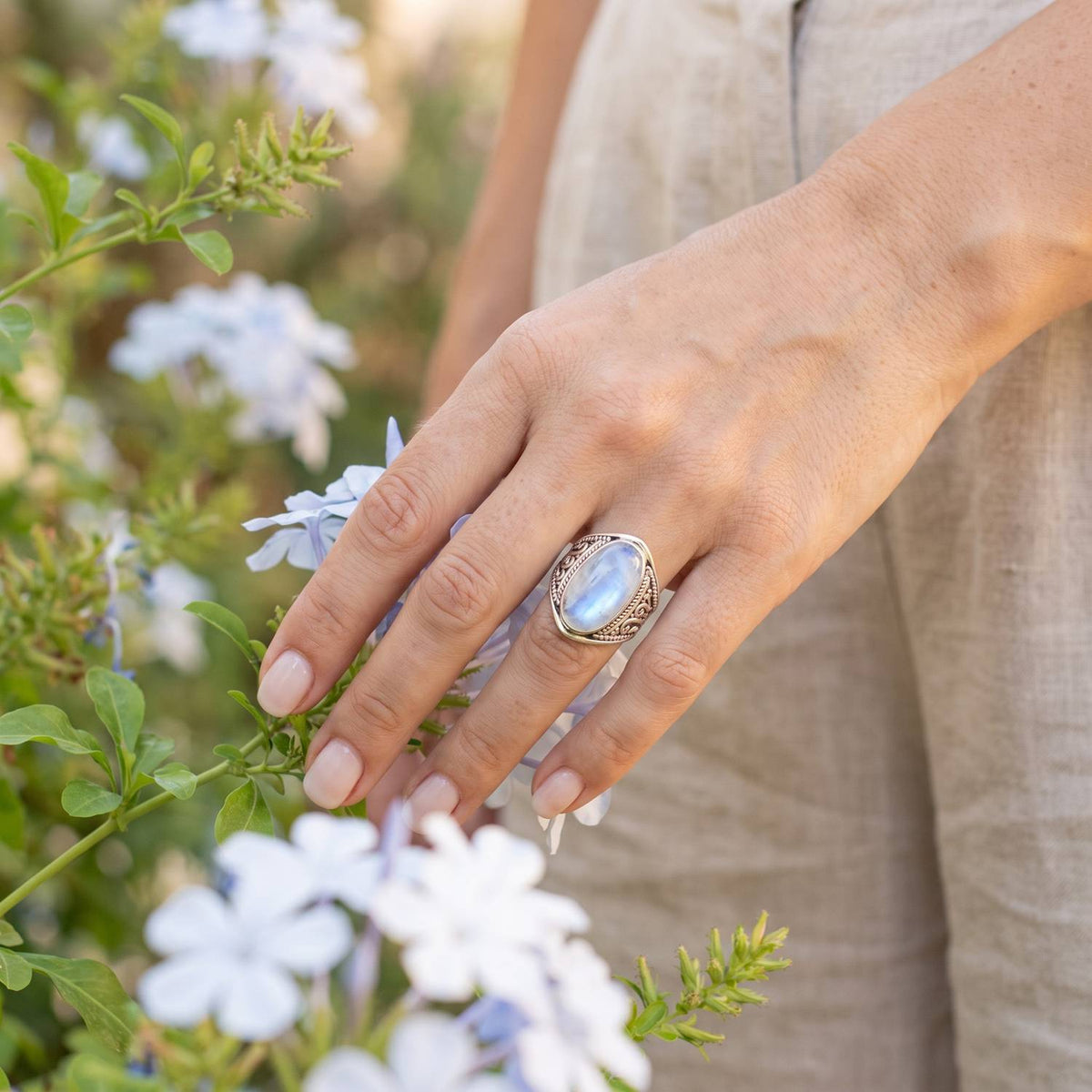 Silberring mit Mondstein an der Hand zwischen Blumen