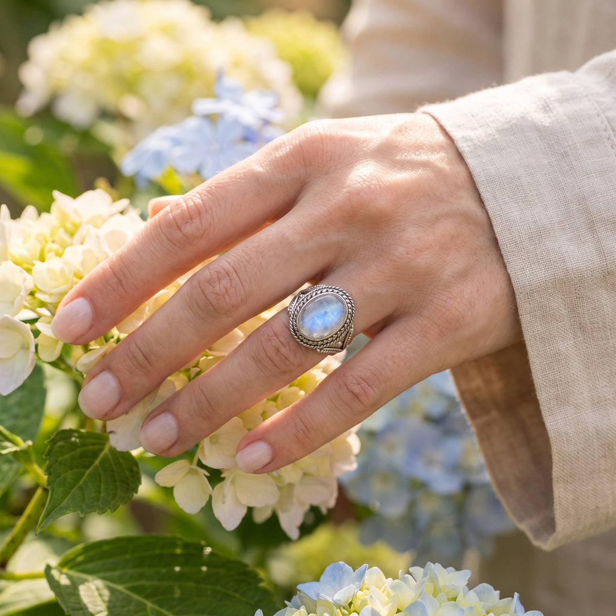 Silberring mit Mondstein an der Hand zwischen Blumen