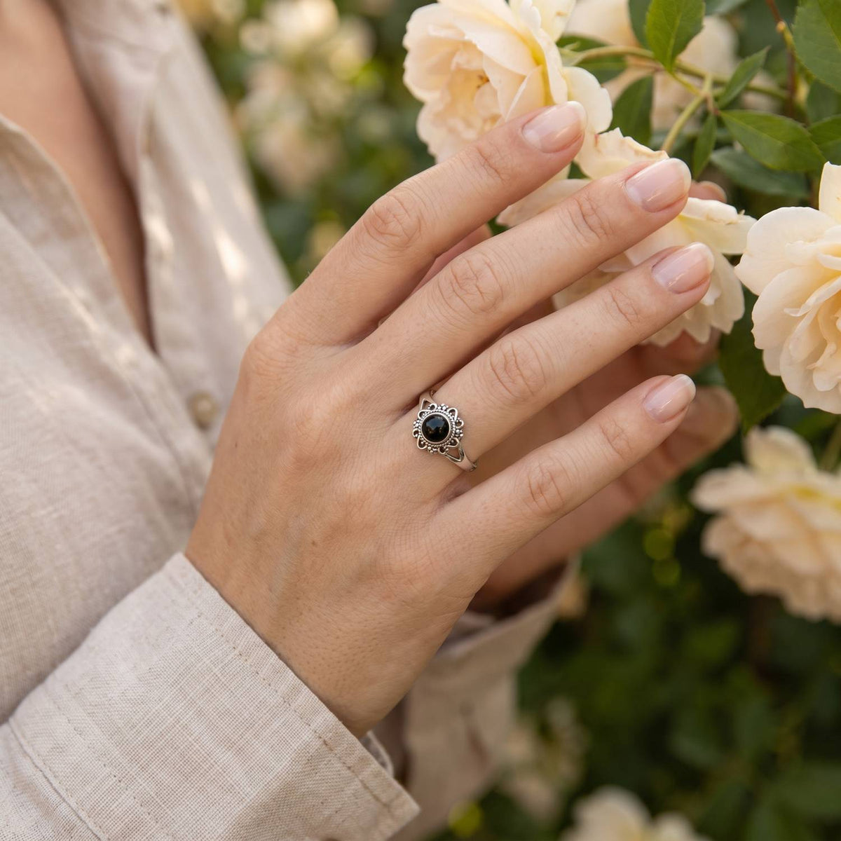 Silberring mit Onyx an der Hand zwischen Blumen