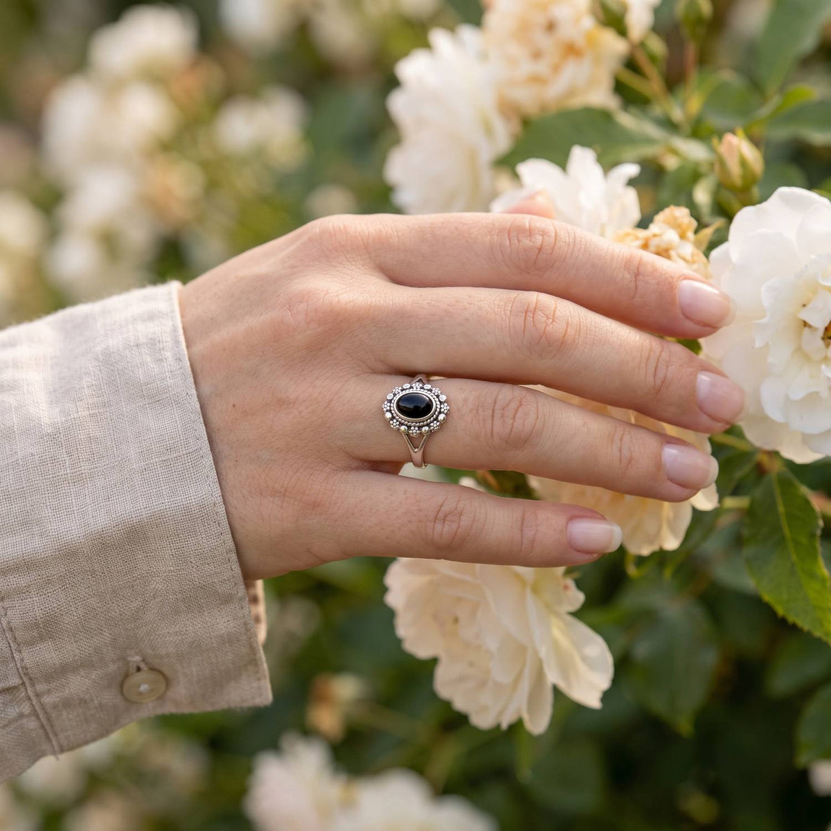 Silberring mit Onyx an der Hand zwischen Blumen