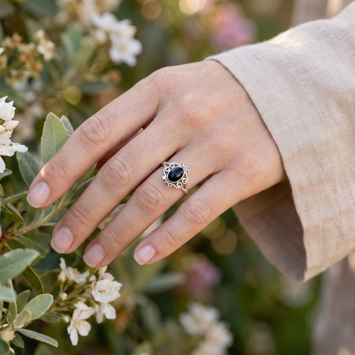 Silberring mit Onyx an der Hand zwischen Blumen