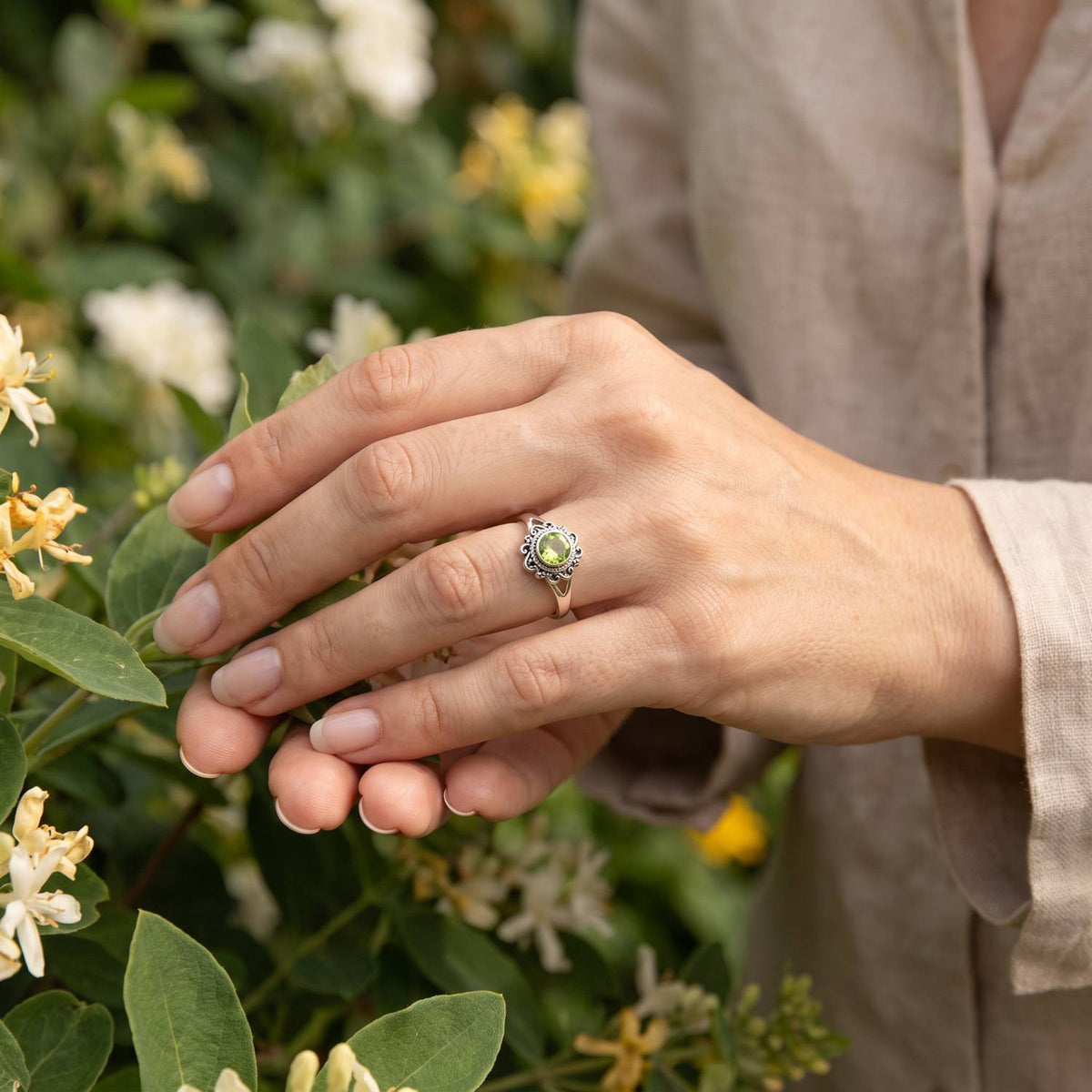 Silberring mit Peridot an der Hand zwischen Blumen