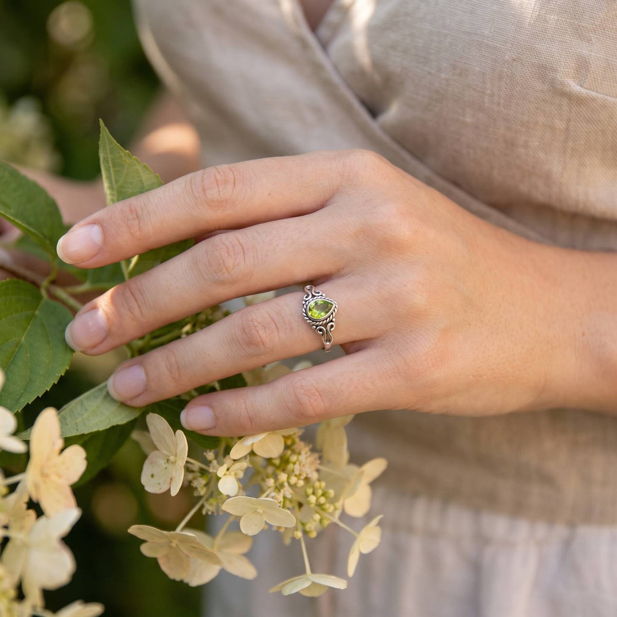 Silberring mit Peridot an der Hand zwischen Blumen