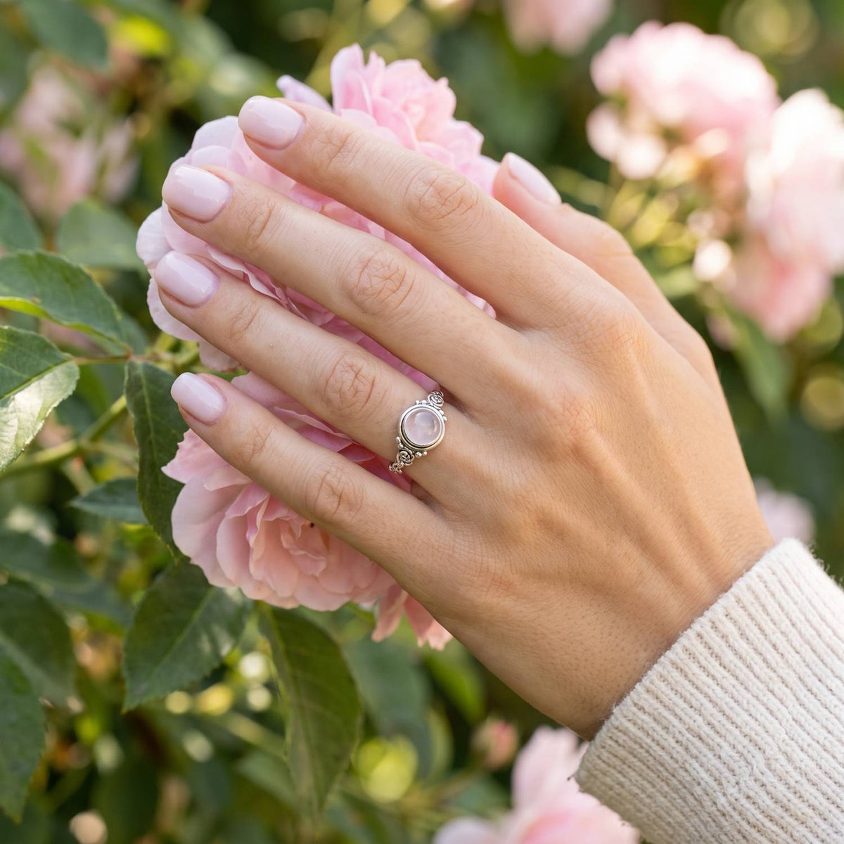Silberring mit Rosenquarz an der Hand zwischen Blumen