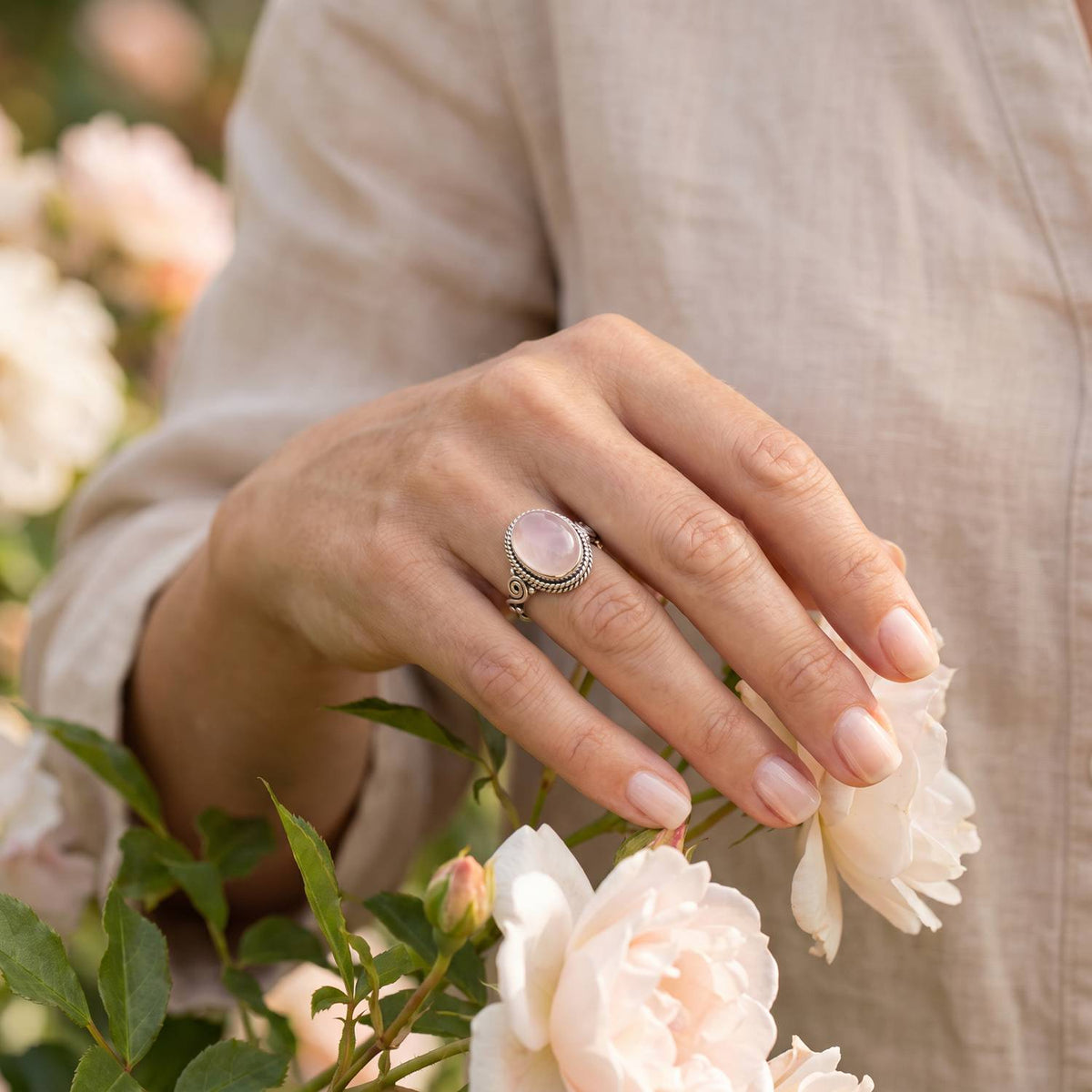 Silberring mit Rosenquarz an der Hand zwischen Blumen
