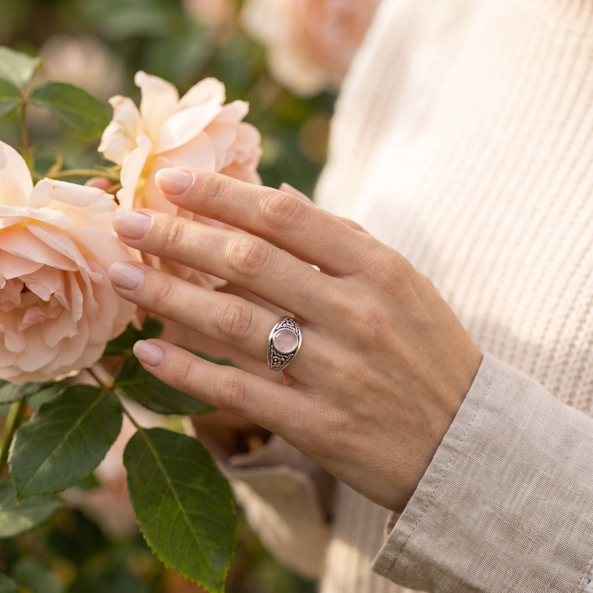 Silberring mit Rosenquarz an der Hand zwischen Blumen