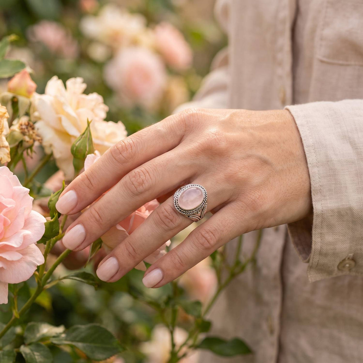 Silberring mit Rosenquarz an der Hand zwischen Blumen