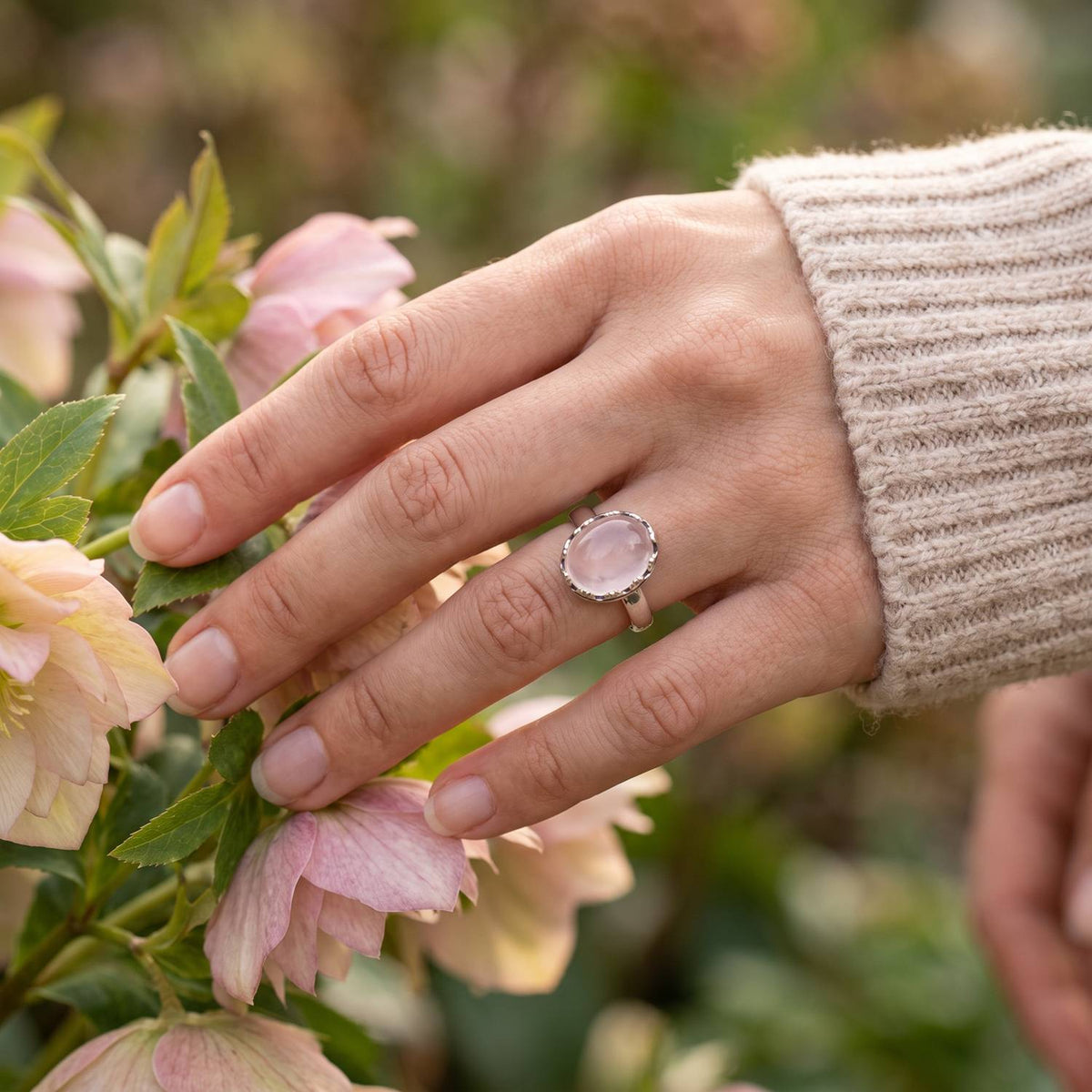 Silberring mit Rosenquarz an der Hand zwischen Blumen