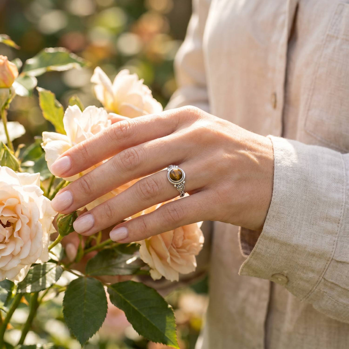 Silberring mit Tigerauge an der Hand zwischen Blumen