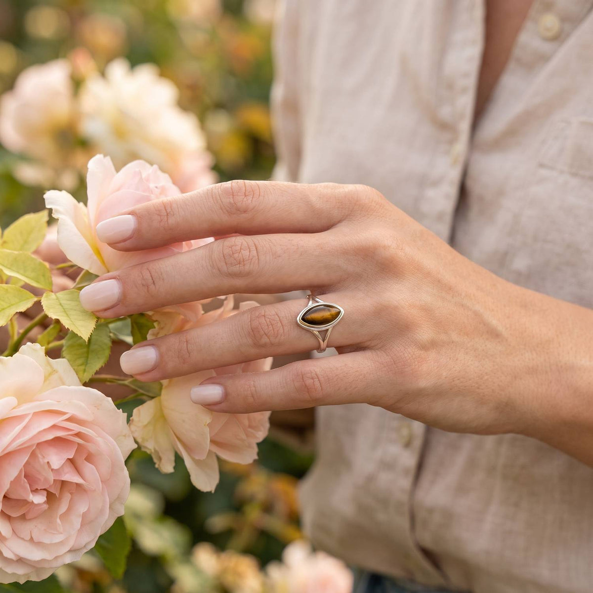 Silberring mit Tigerauge an der Hand zwischen Blumen