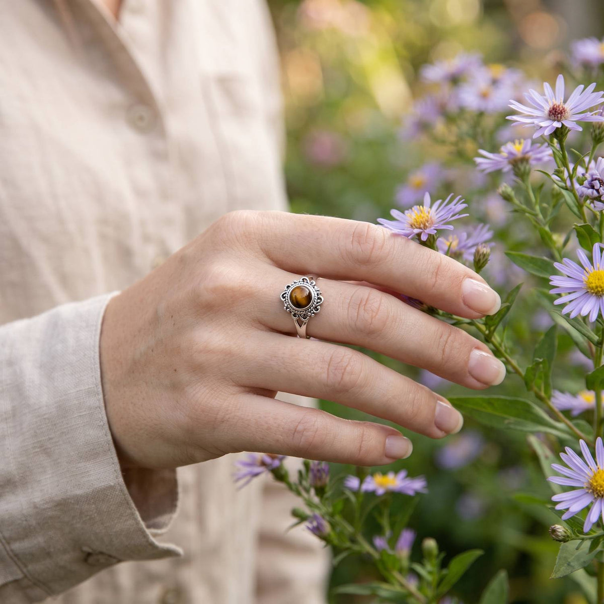 Silberring mit Tigerauge an der Hand zwischen Blumen