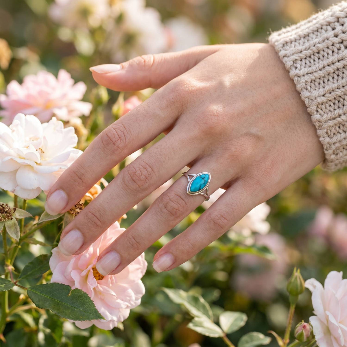 Silberring mit Türkis an der Hand zwischen Blumen