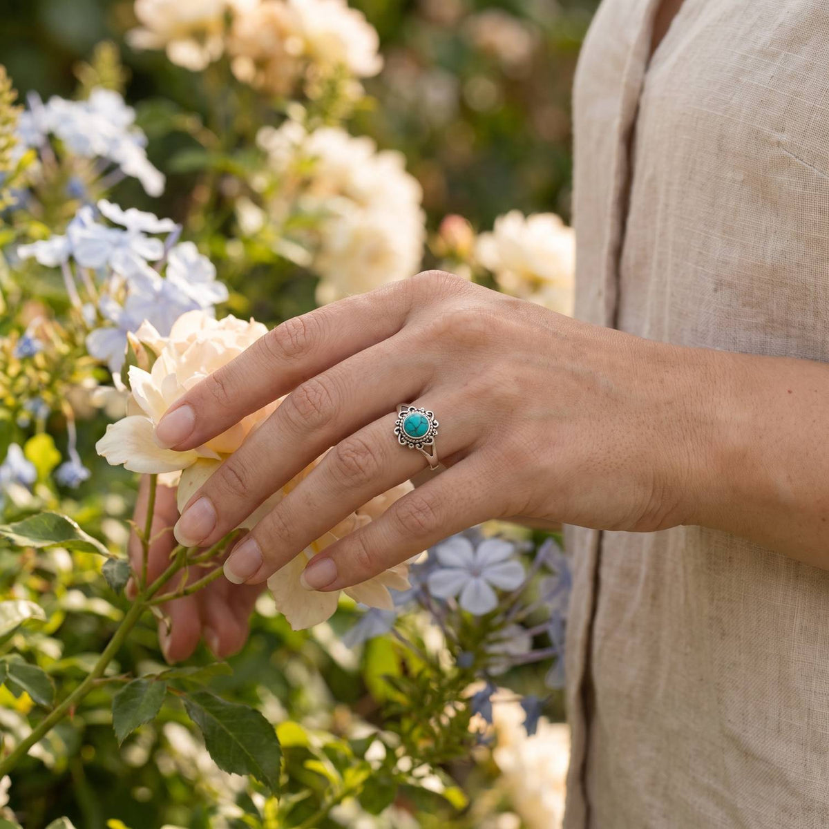 Silberring mit Türkis an der Hand zwischen Blumen