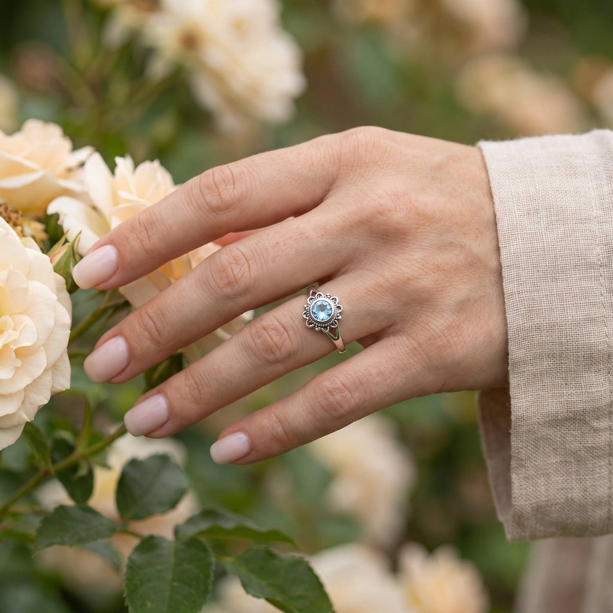 Silberring mit Topas an der Hand zwischen Blumen