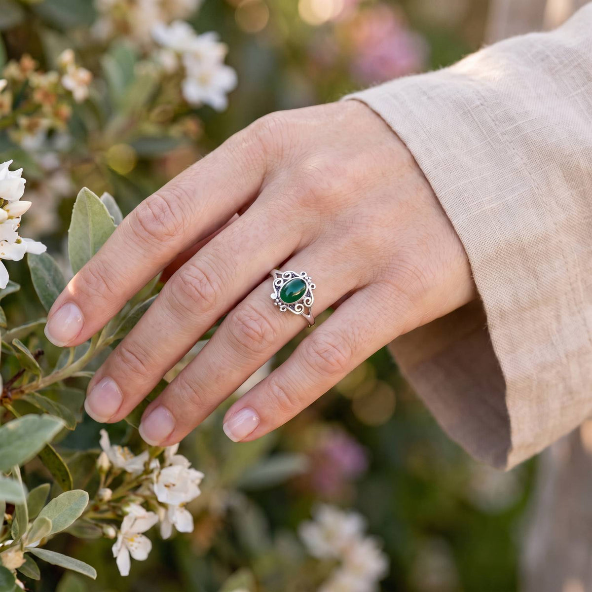 Silberring mit grüner Onyx an der Hand zwischen Blumen