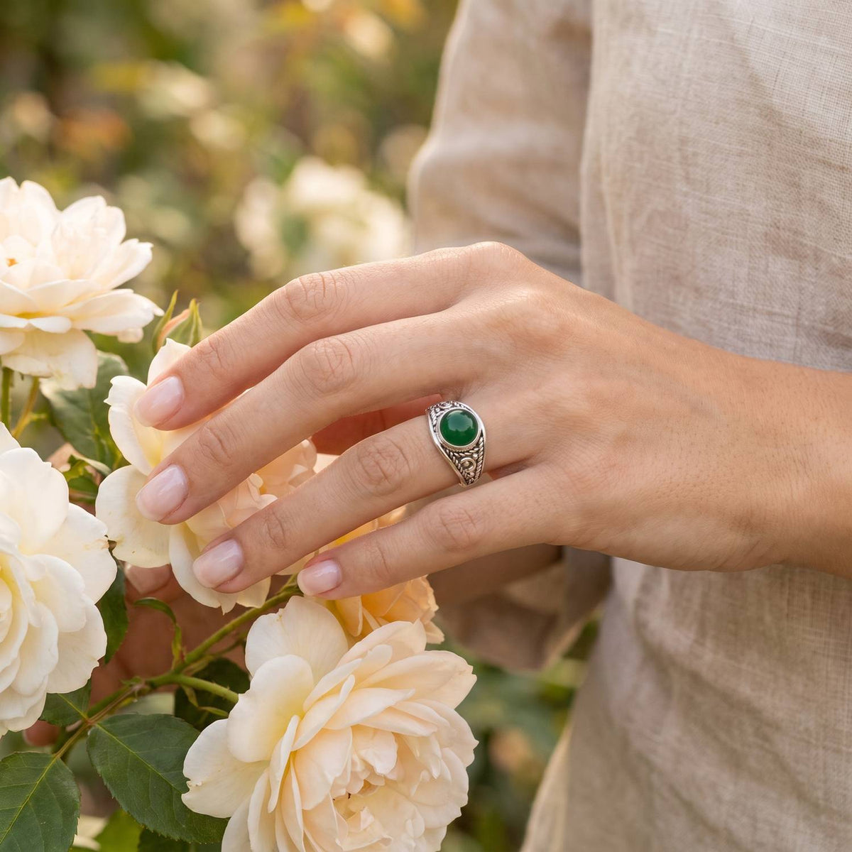 Silberring mit grüner Onyx an der Hand zwischen Blumen