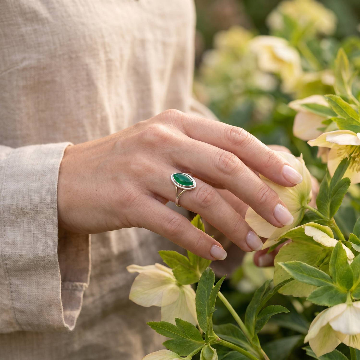 Silberring mit grüner Onyx an der Hand zwischen Blumen