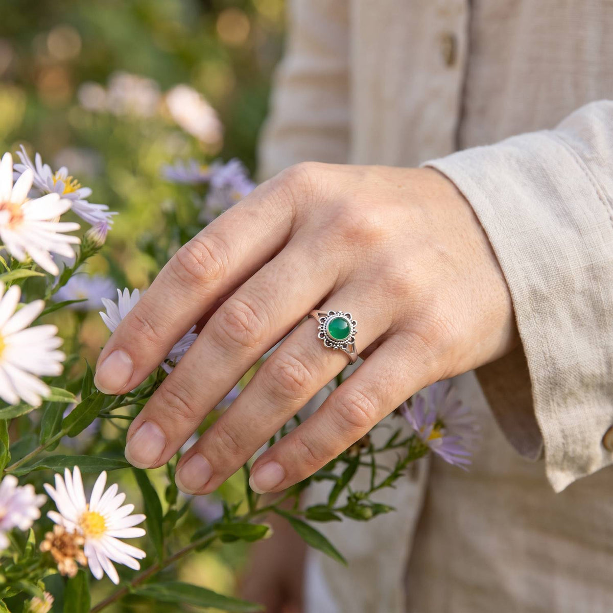 Silberring mit grüner Onyx an der Hand zwischen Blumen