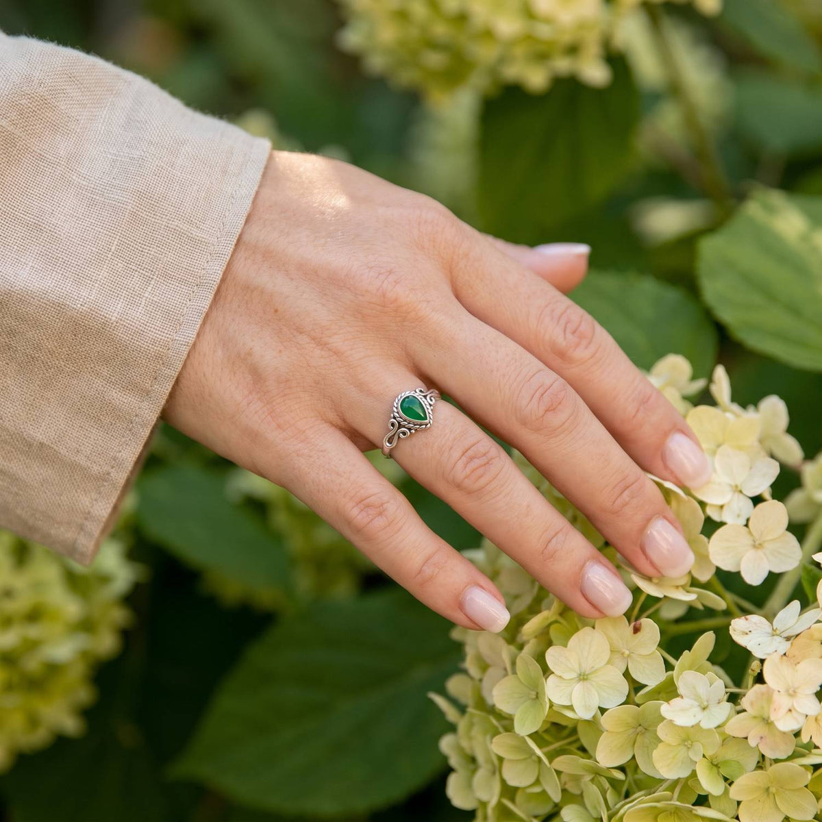 Silberring mit grüner Onyx an der Hand zwischen Blumen