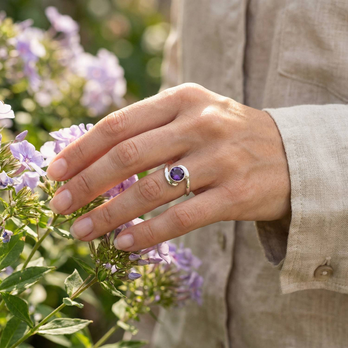Silberring mit Amethyst an der Hand zwischen Blumen