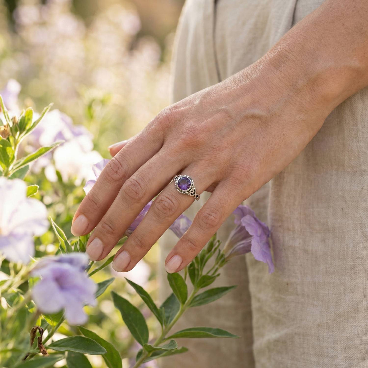 Silberring mit Amethyst an der Hand zwischen Blumen